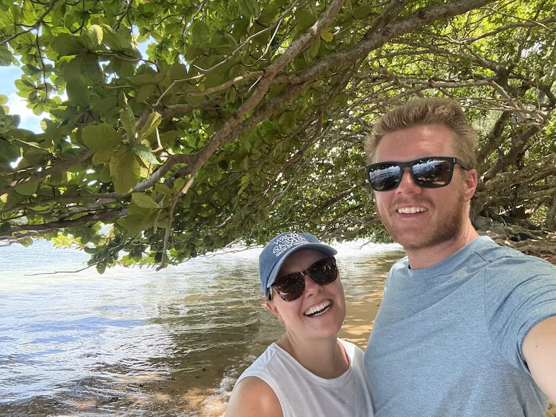 Drew and a companion smiling by the water under leafy trees