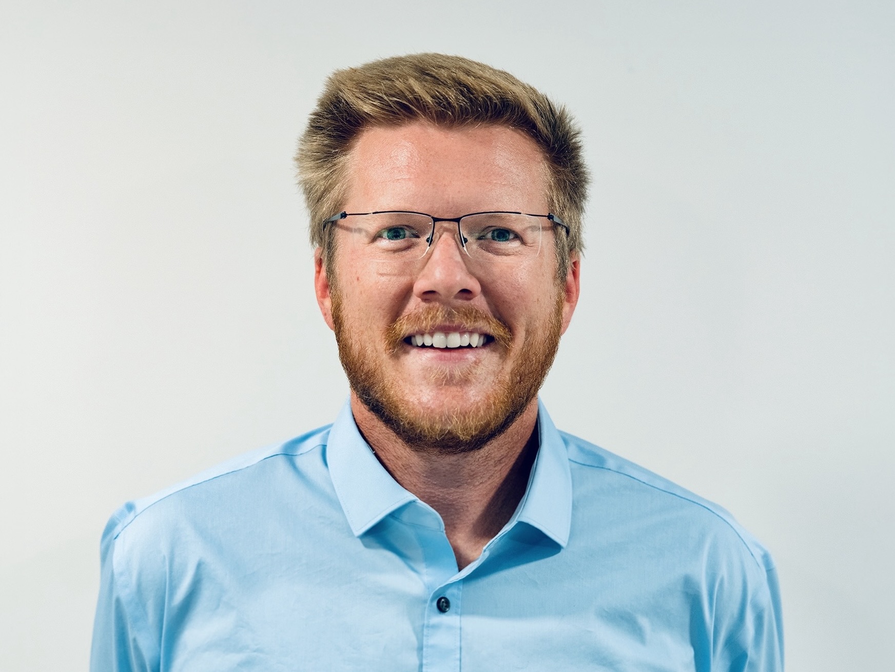 Drew Cotten smiling, wearing glasses and a blue shirt